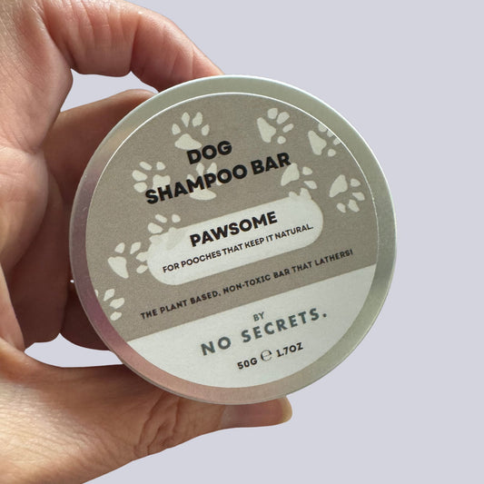Hand holding a dog shampoo bar container labeled 'Pawsome' by 'No Secrets'.
