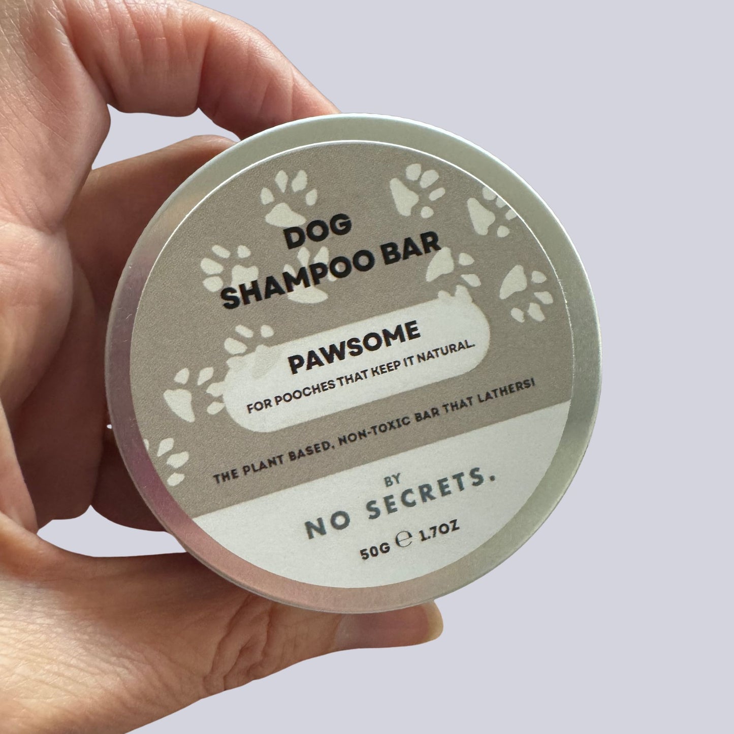 Hand holding a dog shampoo bar container labeled 'Pawsome' by 'No Secrets'.